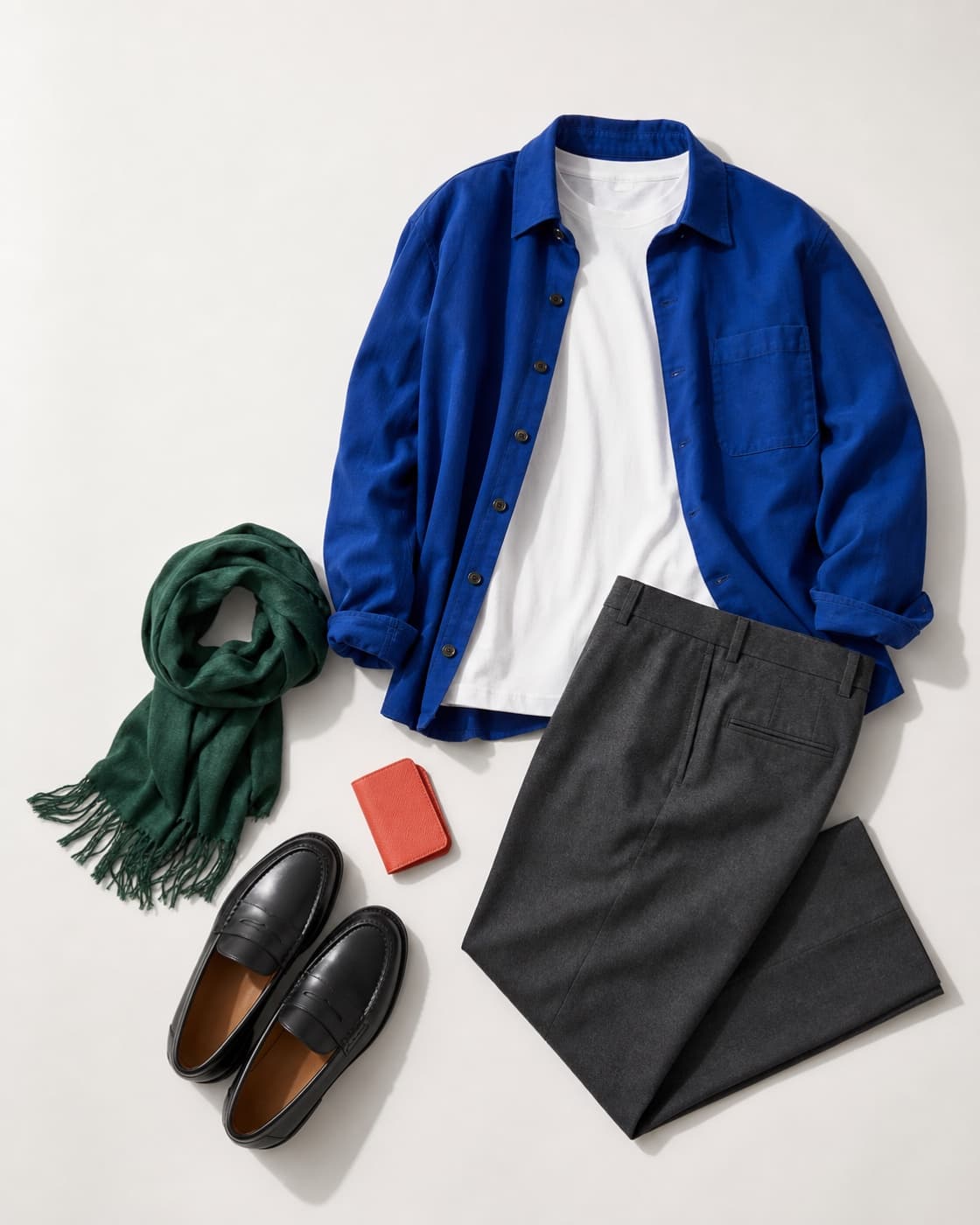 A blue overshirt, white T-shirt, charcoal trousers, green scarf and black loafers arranged as a complete outfit